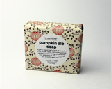 A rectangular bar of La's Sunflower Pumpkin Ale Soap, wrapped in cream-colored paper with a pattern of red pumpkins and dark brown leaves, featuring a large white circular label in the center.